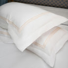 Elegant white pillowcases with golden embroidery stacked on bed