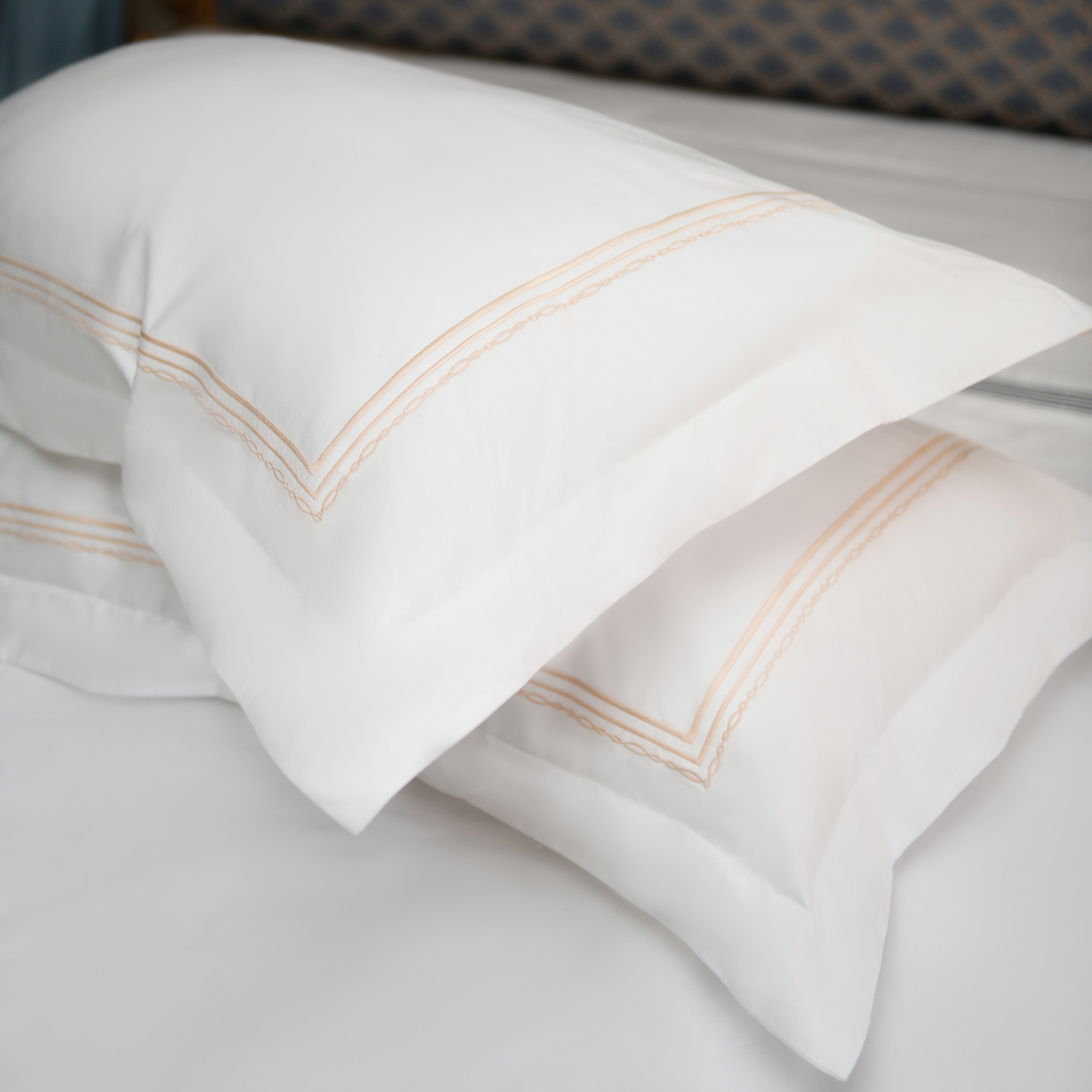 Elegant white pillowcases with golden embroidery stacked on bed