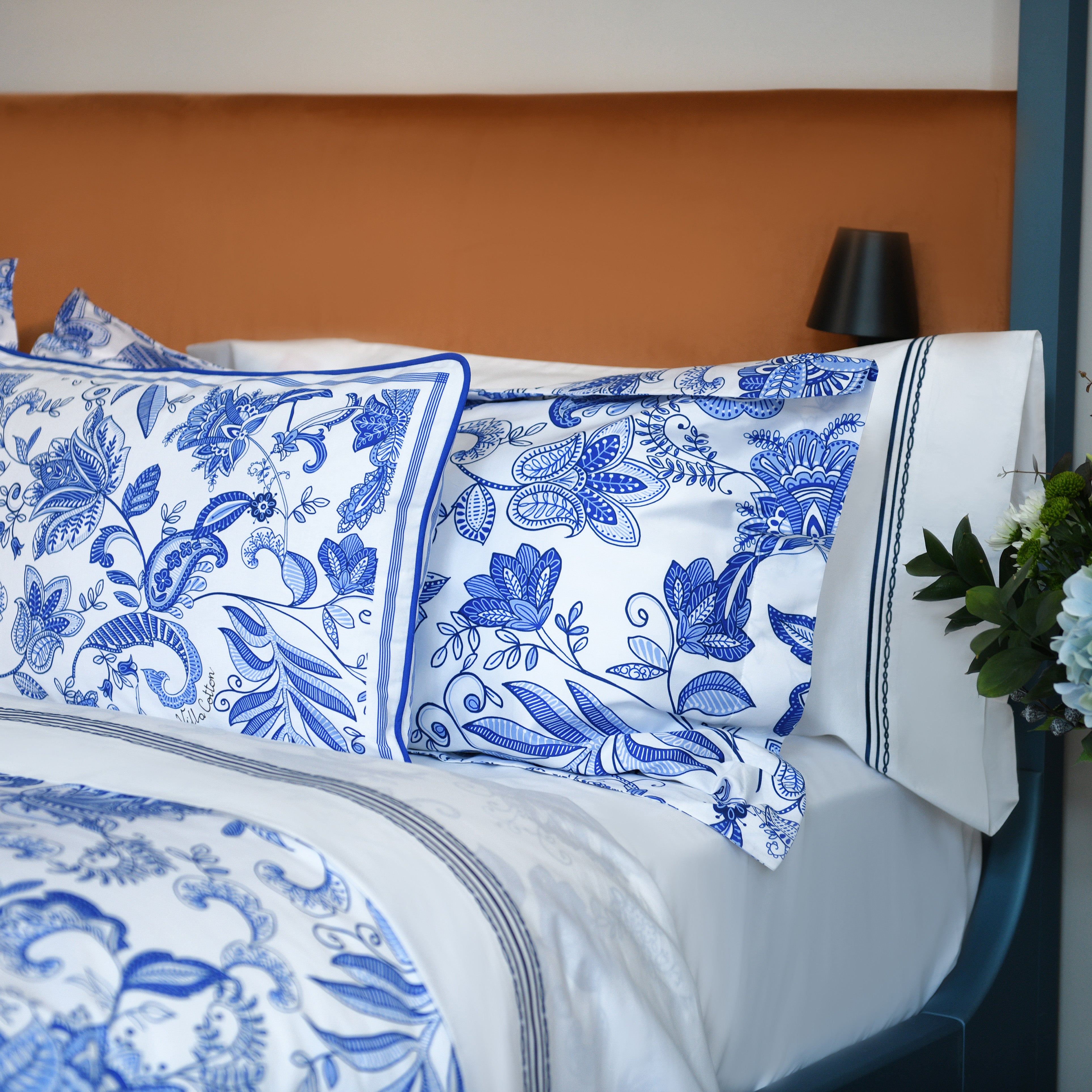 Oxford pillowcases with intricate blue print on soft cotton bedding, set against warm velvet headboard