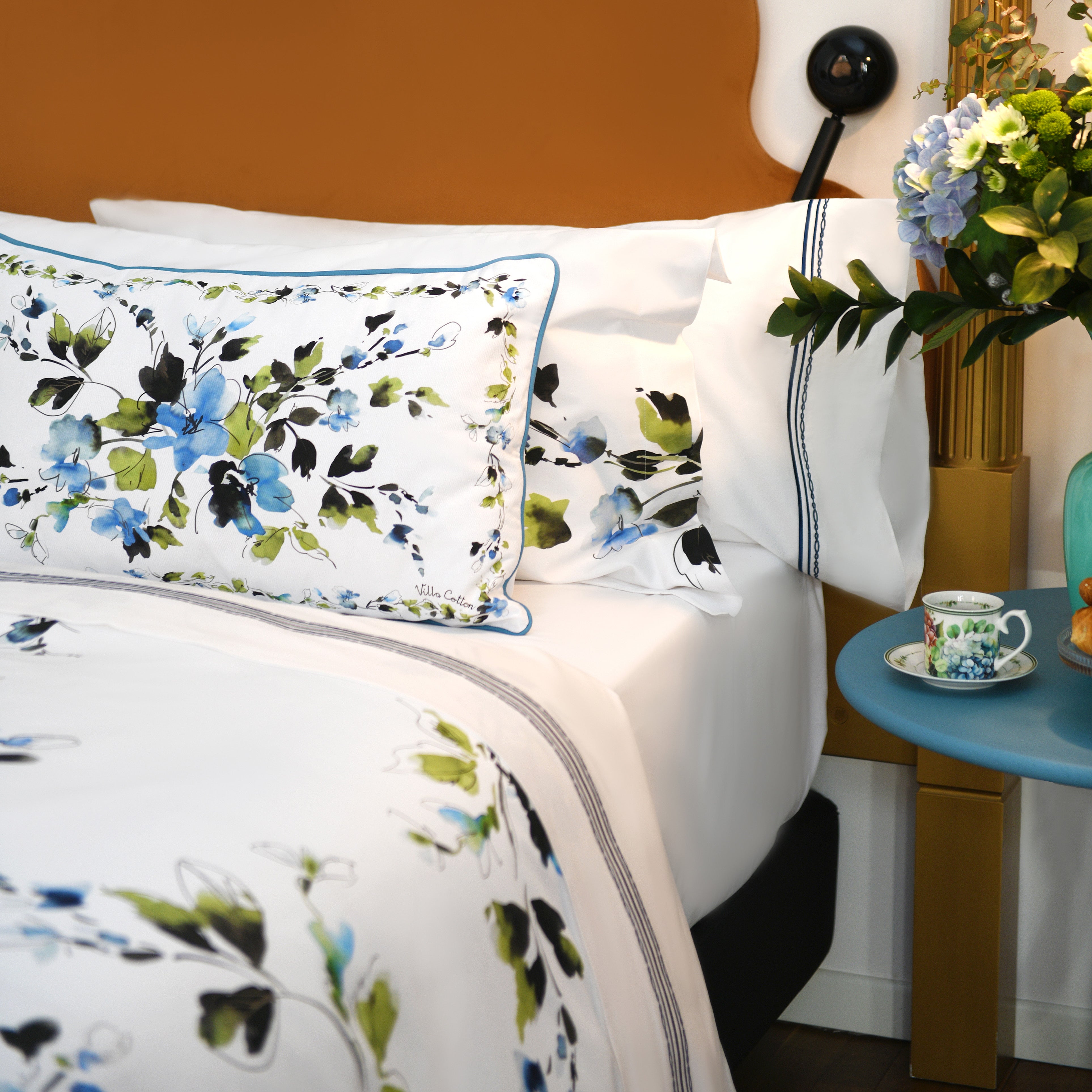 Close-up of Primavera floral shams on white cotton bedding with blue, green, and black watercolor-style flowers
