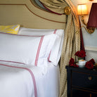 Close-up of Oxford shams with ruby red embroidery on white cotton bedding, red roses and warm lighting
