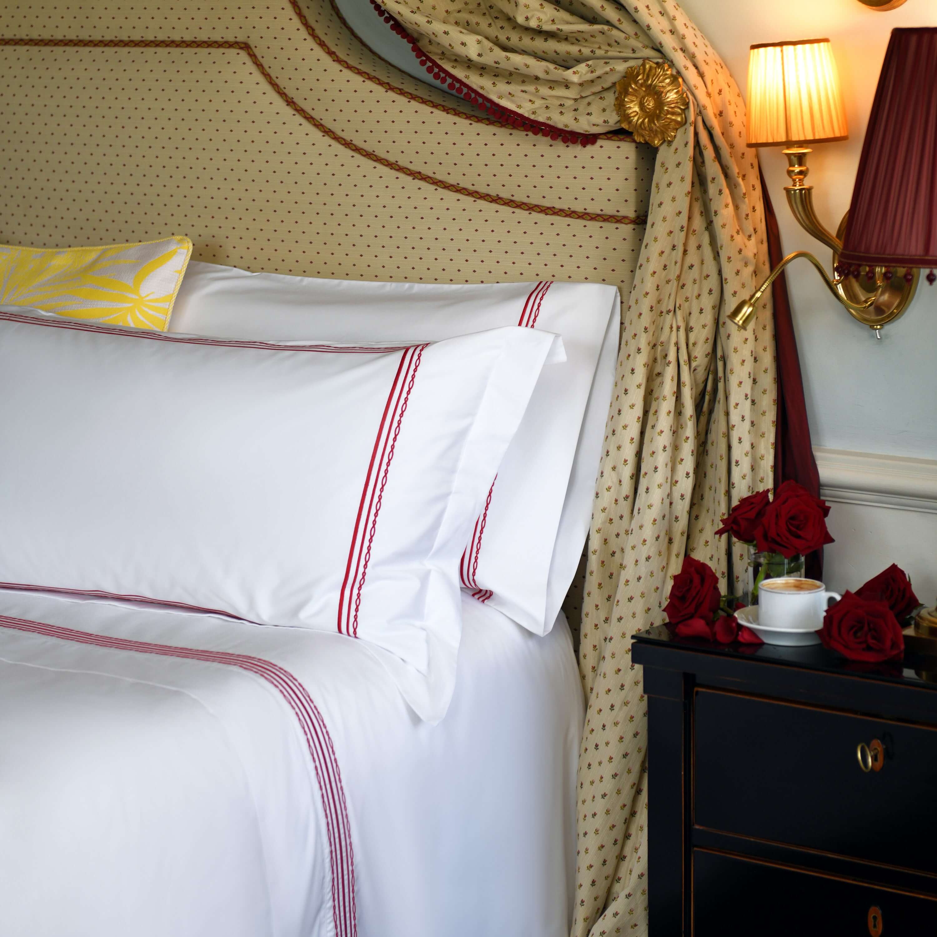 Close-up of Oxford shams with ruby red embroidery on white cotton bedding, red roses and warm lighting
