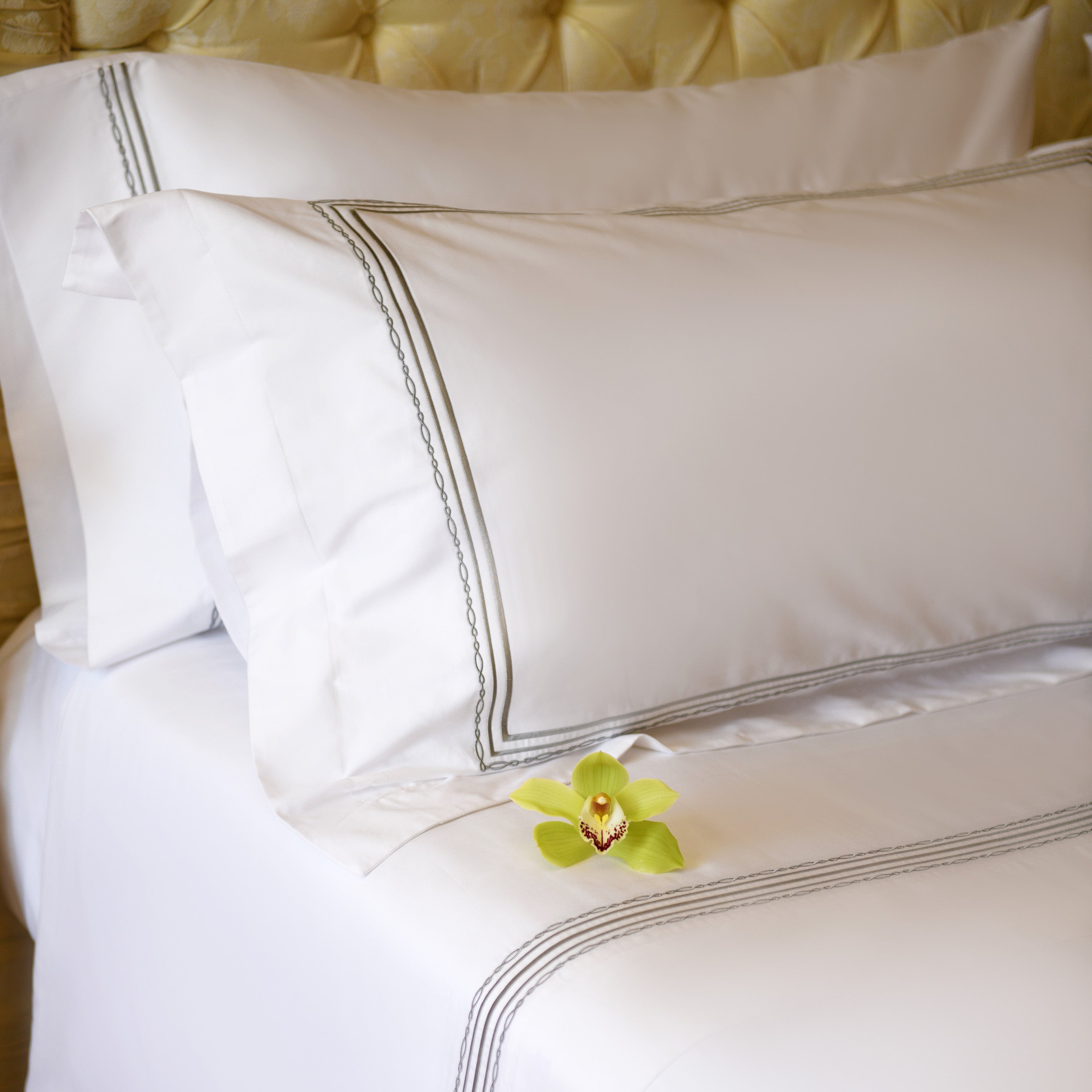 Elegant white pillowcases with silver embroidery and green orchid on bed
